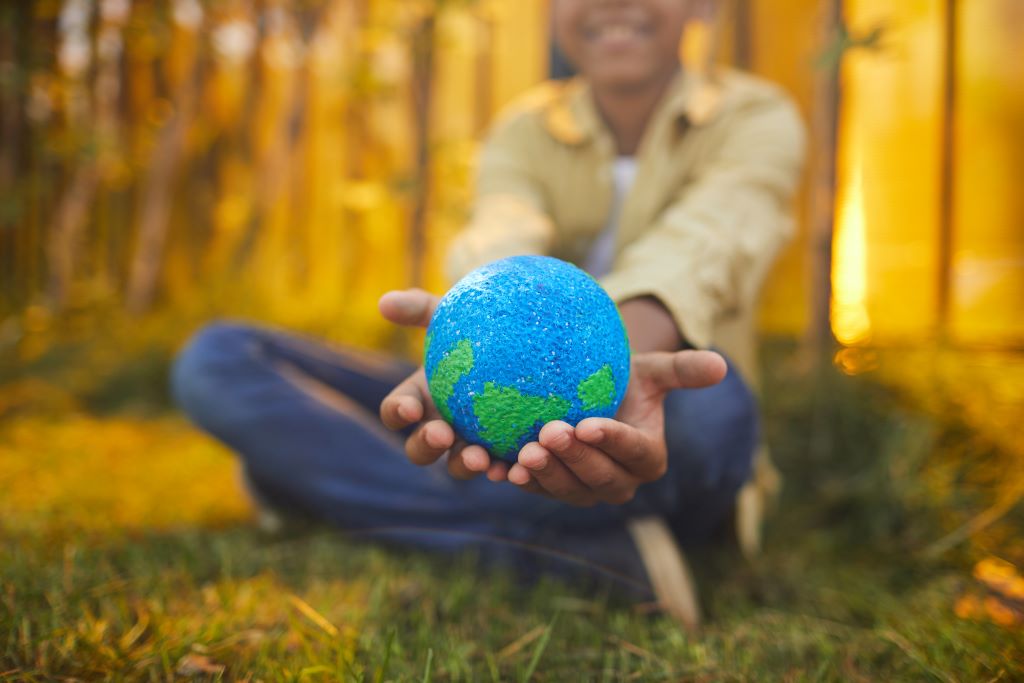 Boy in a woodland holding out a model of planet earth